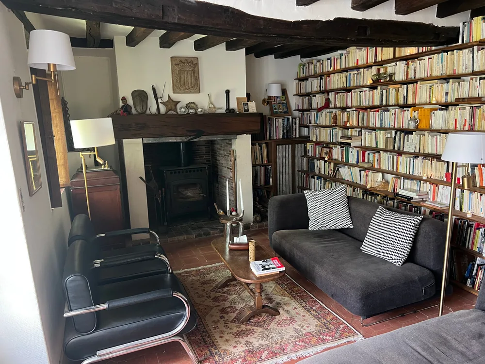 La grande bibliothèque du Couvent : poutres, poêle dans la cheminée, canapé et murs de livres