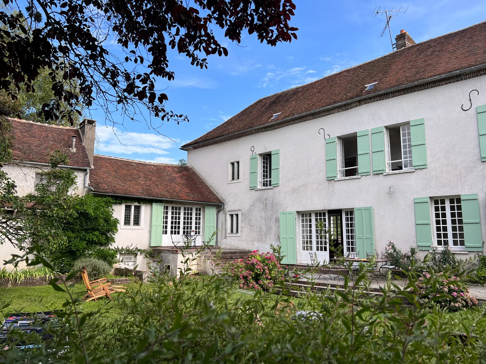 Le Couvent côté jardin : façade blanche, volets vert d'eau, terrasse et hortensias